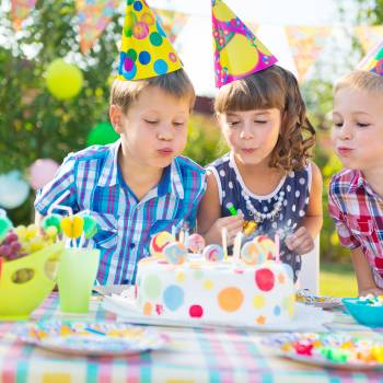 Kids Blowing Candles On Cake At  Birthday Party Kids celebrating birthday party and blowing candles on cake